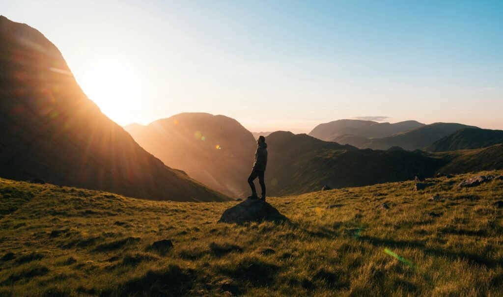 Traveler standing on mountain peak overlooking a scenic landscape at sunrise, symbolizing adventure and travel inspiration